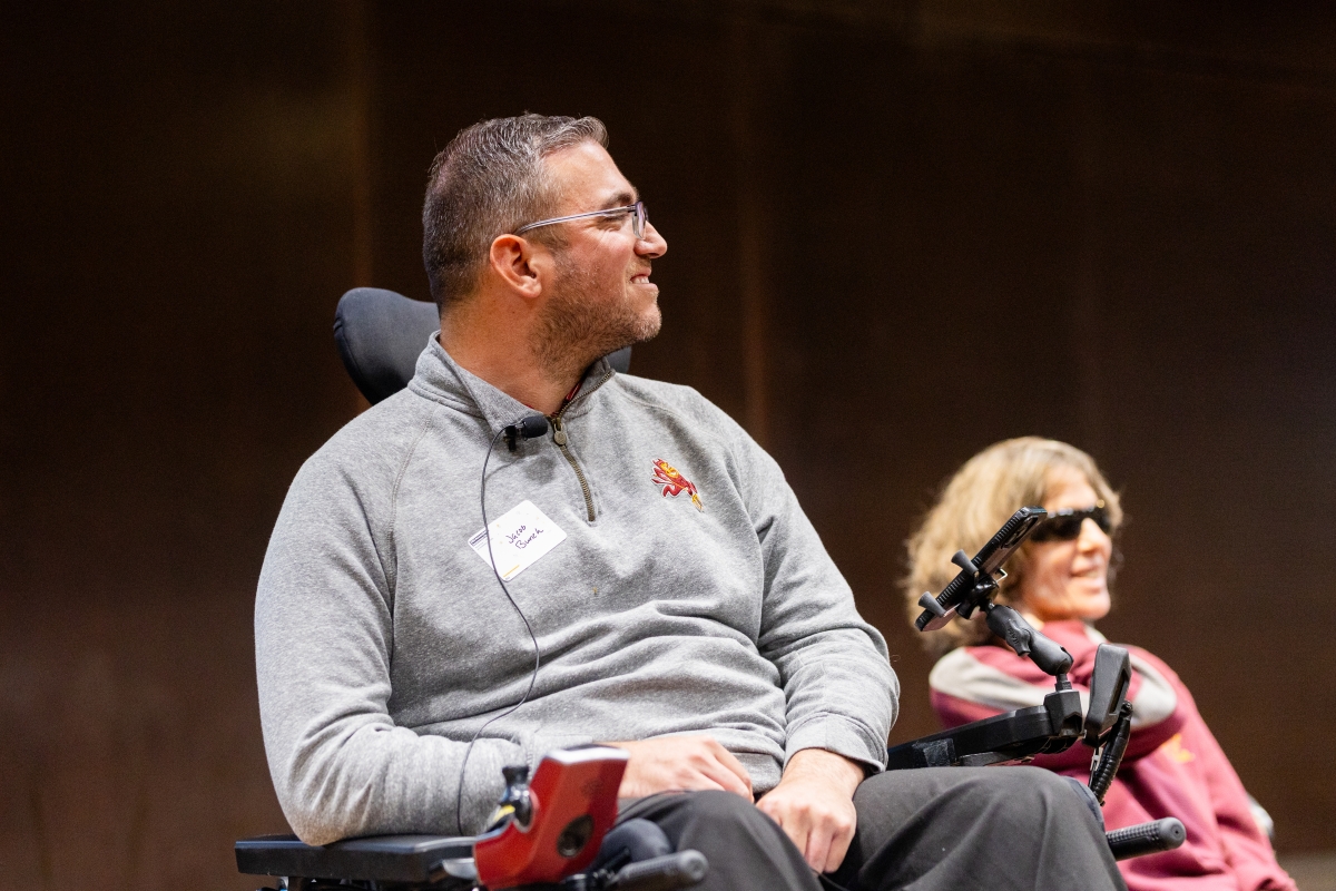 Man in grey shirt, and in a wheelchair, is looking to his side with a woman in the background