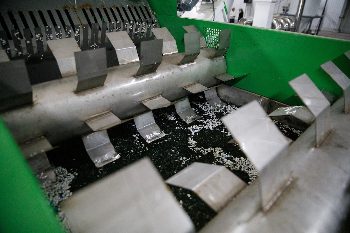 Close-up of an industrial machine with metal blades and scattered plastic pieces inside.