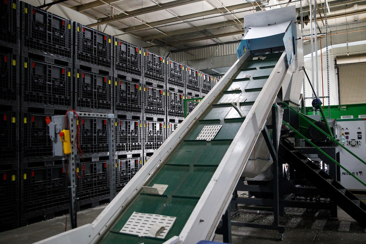 Inclined green conveyor belt in an industrial setting with plastic crates and a control panel.