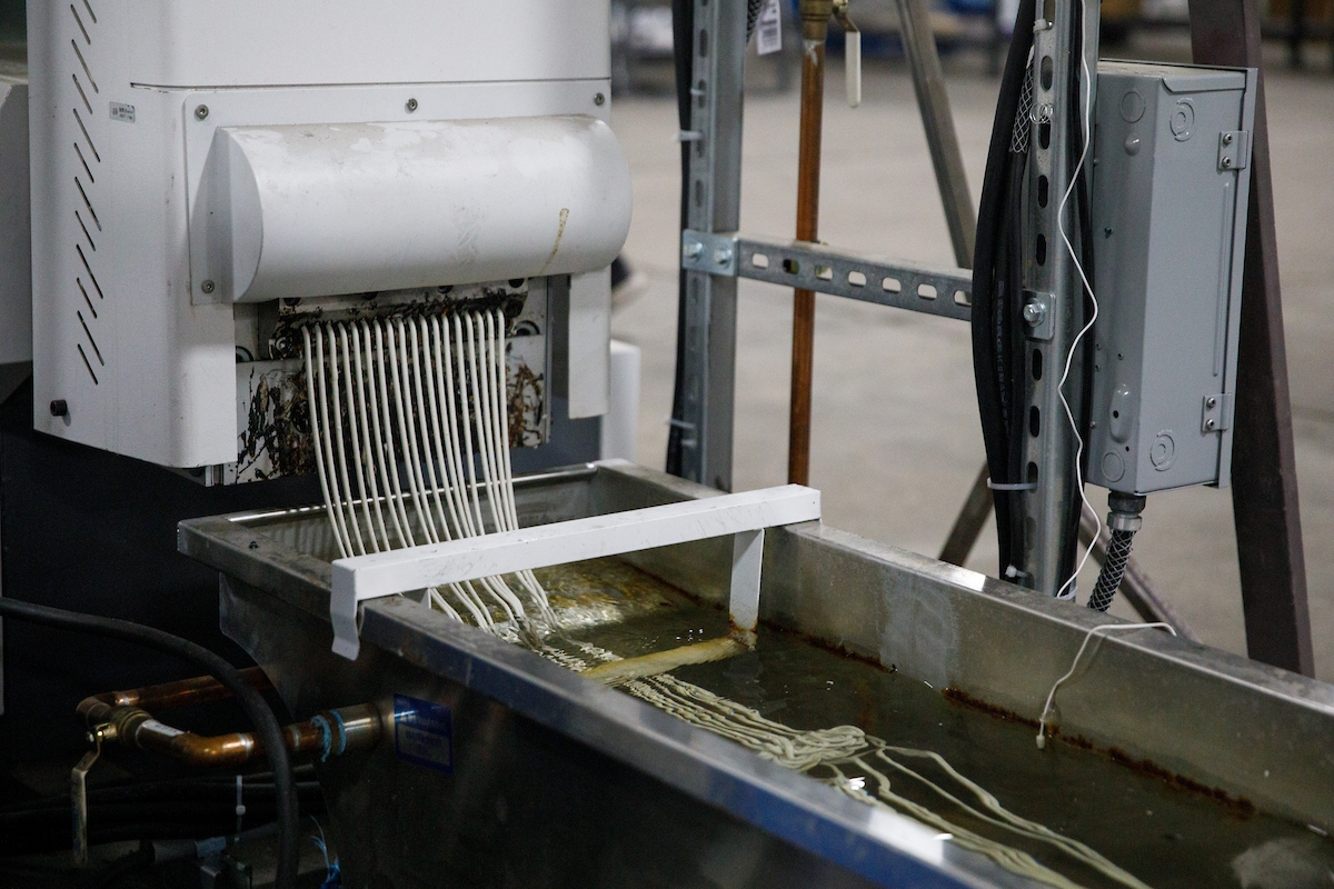 Machine extruding noodle-like plastic material into a liquid-filled trough.