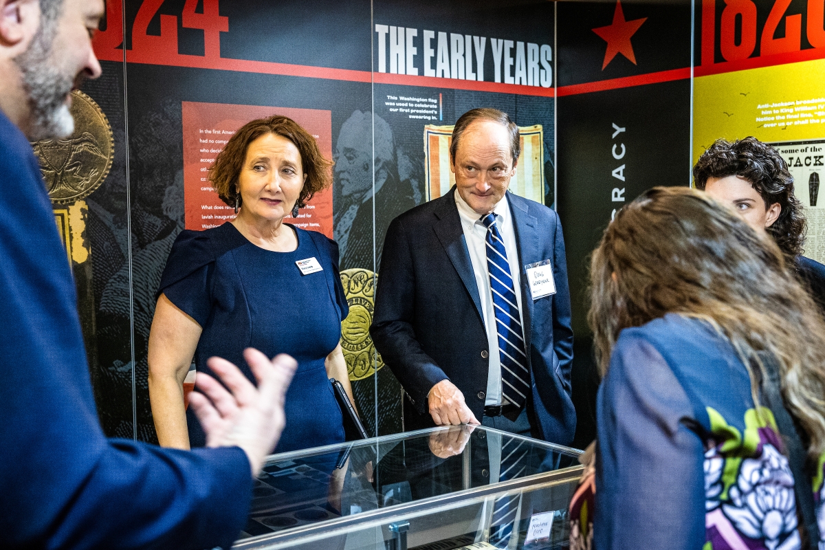 Group of people stand around display case at exhibit event