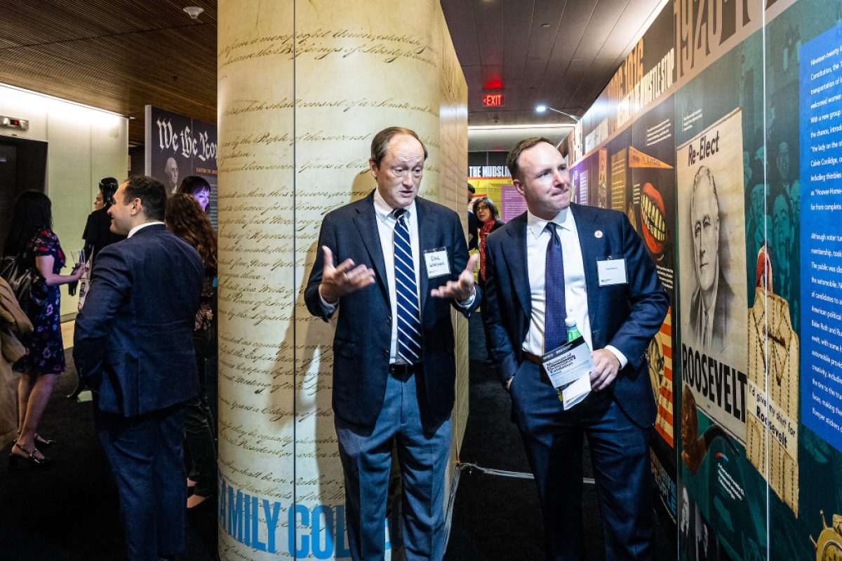 Two men in suits and ties look at wall displays at exhibit