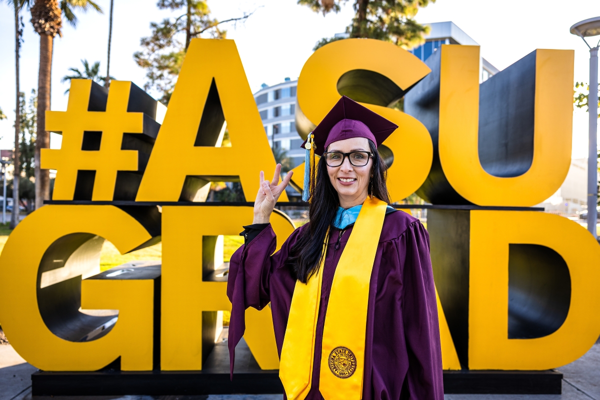 A graduate poses in front of a giant gold sign that reads ASU Grad