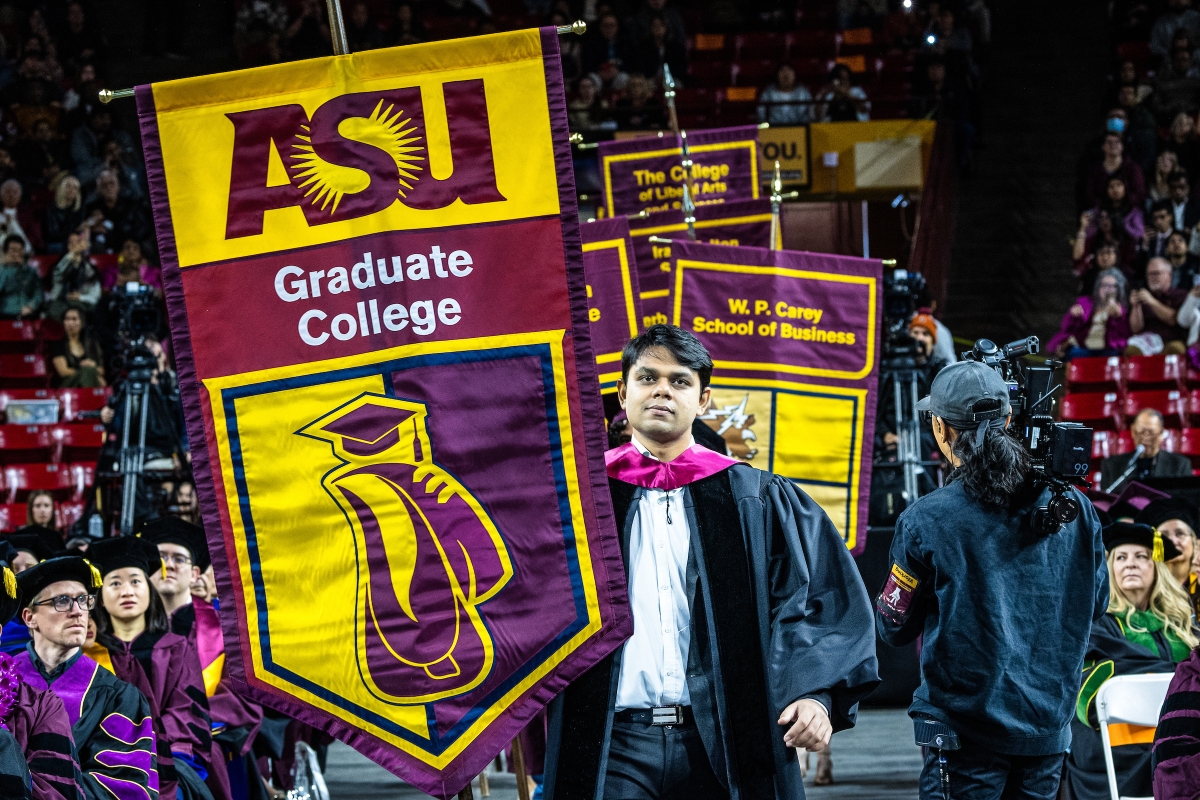 A graduate student carries a gonfalon that says ASU Graduate College into commencement