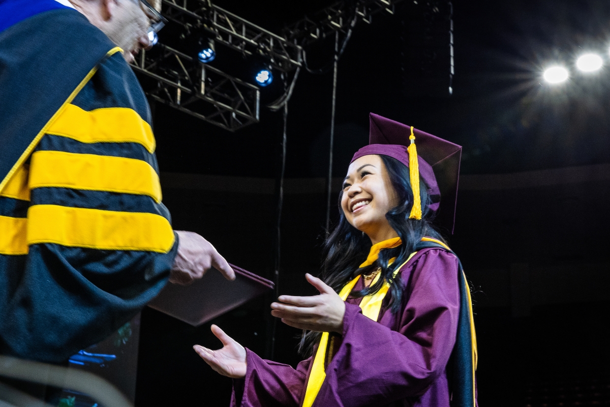 A student in graduation regalia receives a diploma cover onstage