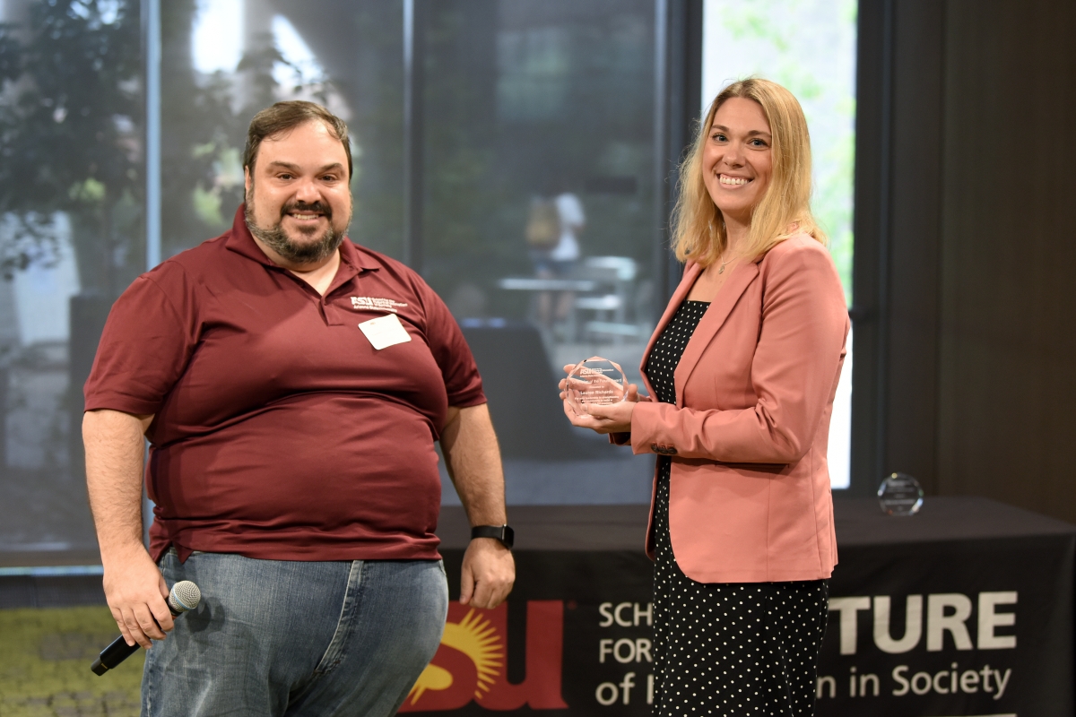 Man holding a microphone and woman holding an award smiling.