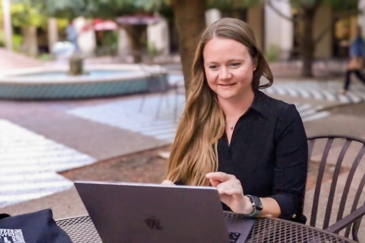 Woman working on a laptop in a courtyard.