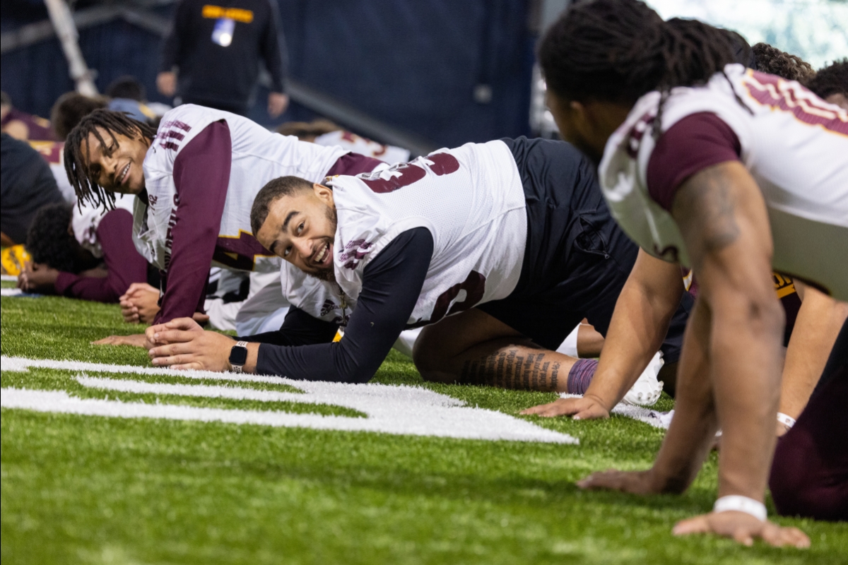 ASU football players smile as they stretch on the ground