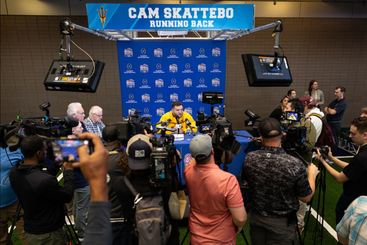 An ASU football player speaks into a mic with dozens of cameras and reporters surrounding him