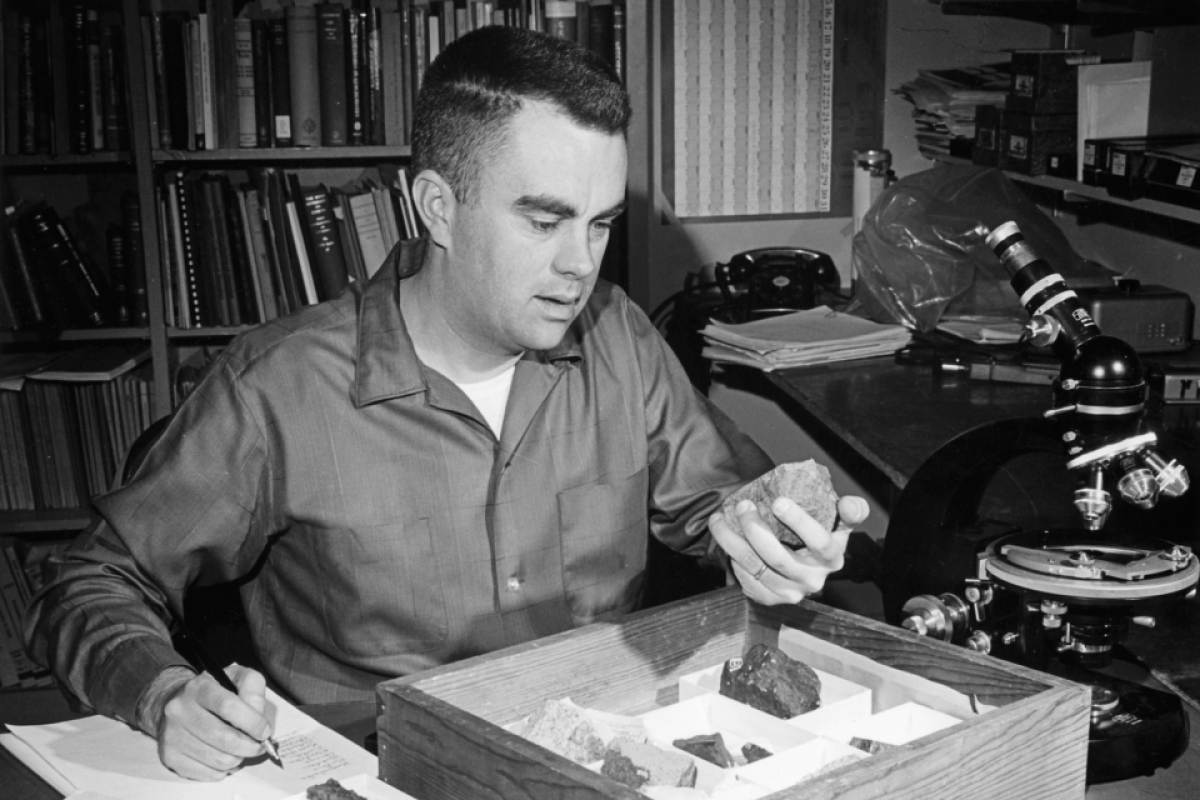 Black and white photo of a man in a button up shirt looking through a box of meteorites in an office