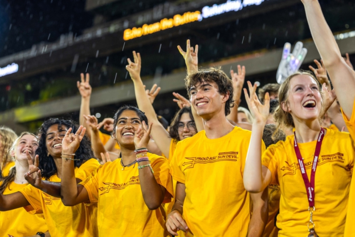 Students cheering in gold t-shirts at ASU football stadium in the rain