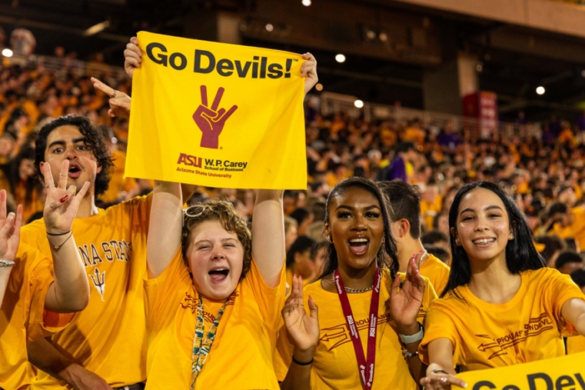 Students wearing gold t-shirts at football stadium hold up Go Devils banner