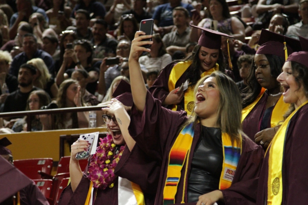 A graduate stands in a crowd taking a selfie.