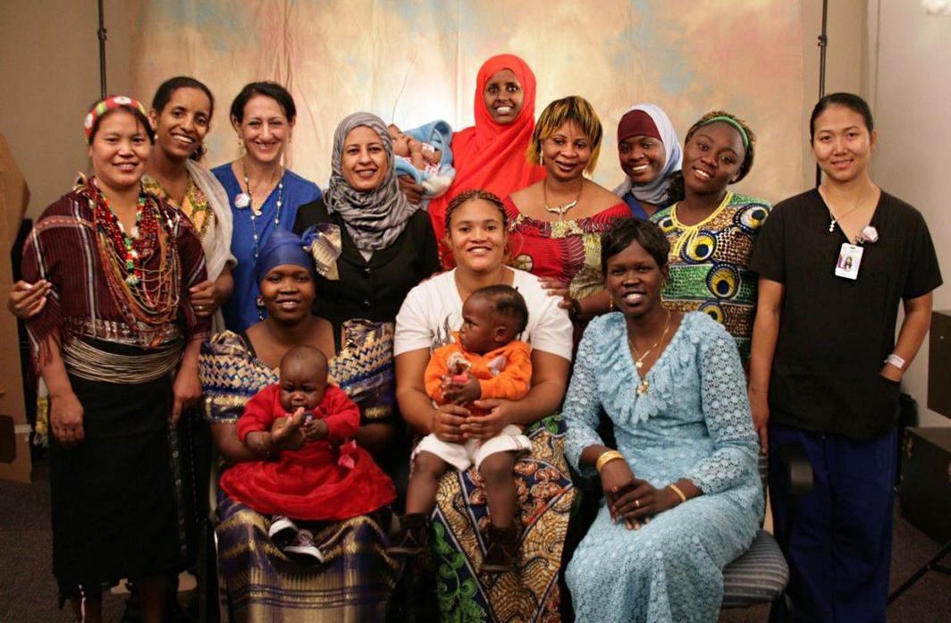 Group of 12 RWHC staff and refugee mothers with 3 babies smiling in front of backdrop
