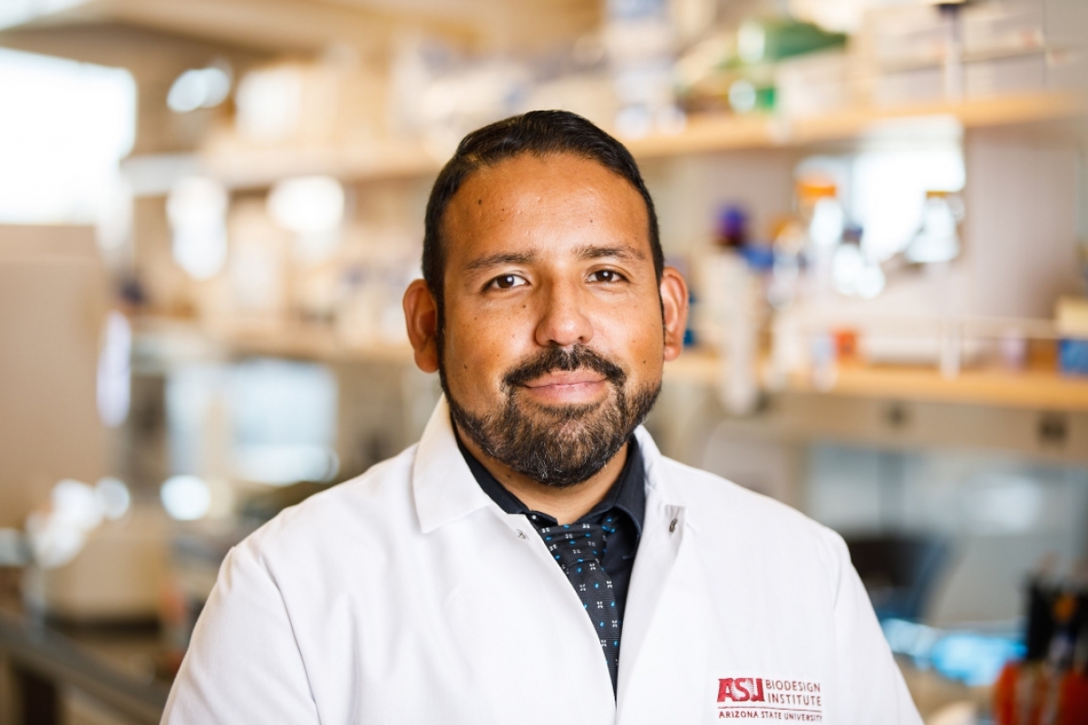 Ramon Velazquez, researcher in the ASU-Banner Neurodegenerative Disease Research Center at the Biodesign Institute, smiles for a portrait while wearing a white coat in a lab 
