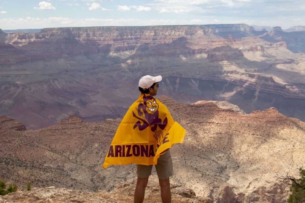 Student from ASU-Cintana Summer Immersion Program poses at the Grand Canyon wrapped in an ASU Sparky flag.