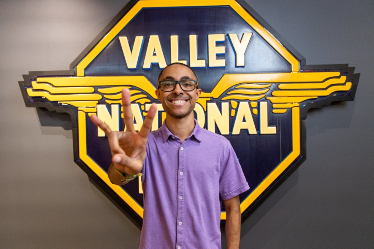 Man making the ASU pitchfork symbol and standing in front of a large business sign that reads "Valley National Bank."