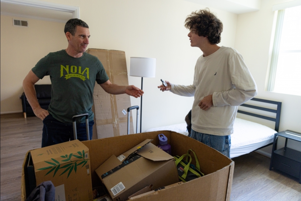 Two men in an apartment with moving boxes visible in the front