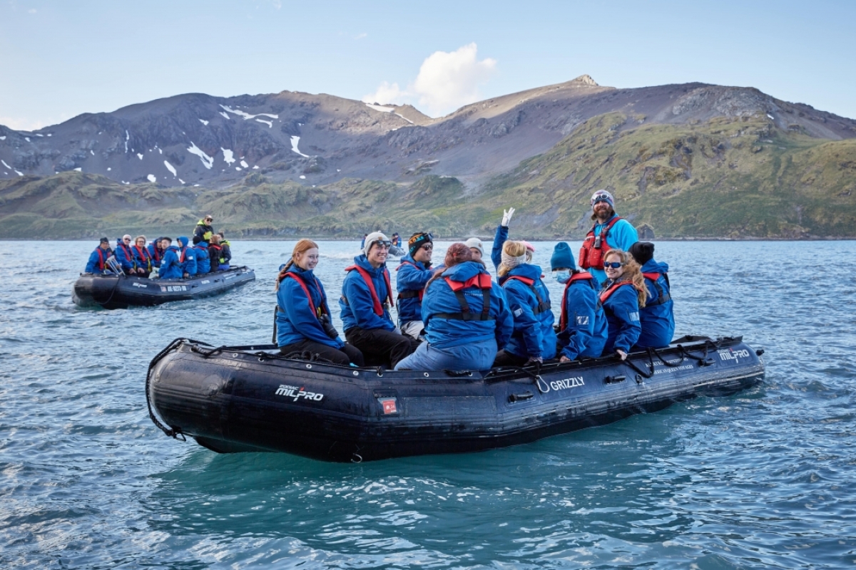 Groups of students on large rafts in an ocean with mountains in the background.