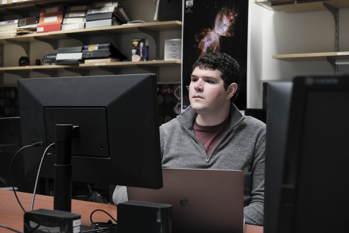 Man seated at a desk looking at a computer monitor.