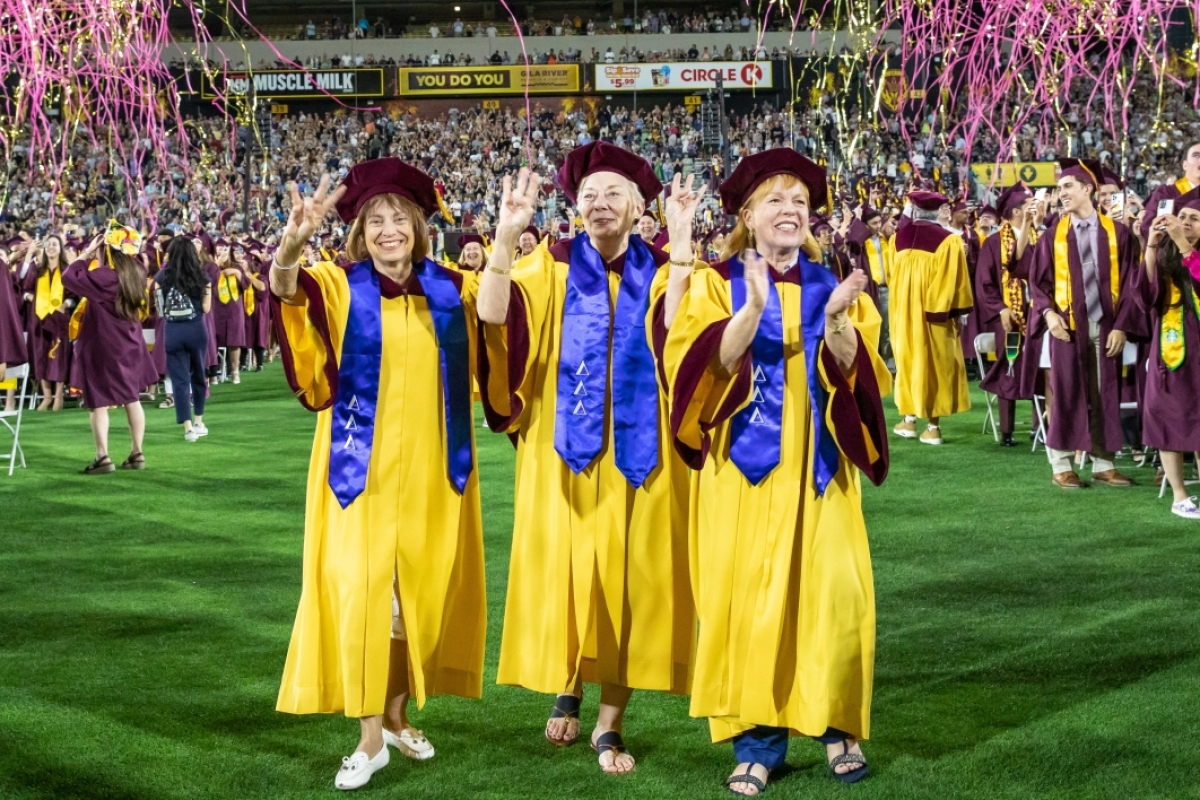 Three Tri Delta sorority sisters and Golden Graduates stand together clapping and doing the forks-up sign.
