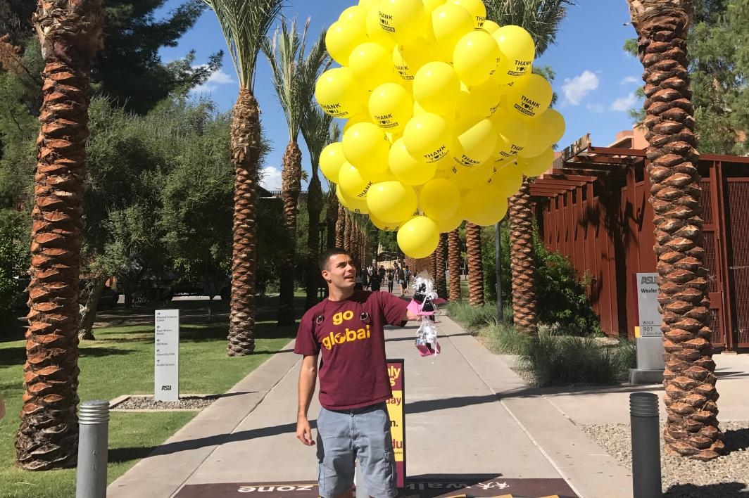 Student holds a bunch of 50 yellow balloons at Palm Walk
