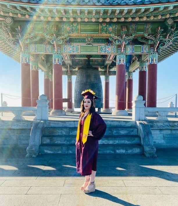 woman wearing cap and gown in front of a temple