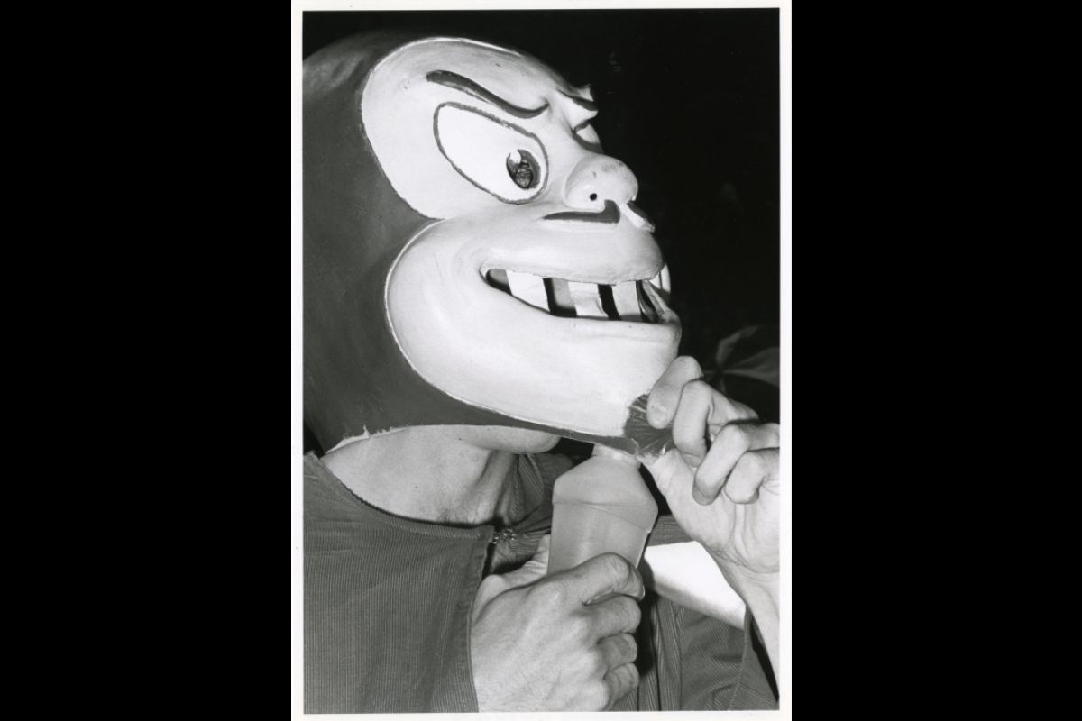 A black and white photo of the Sparky mascot holding the mask up to get a drink of water