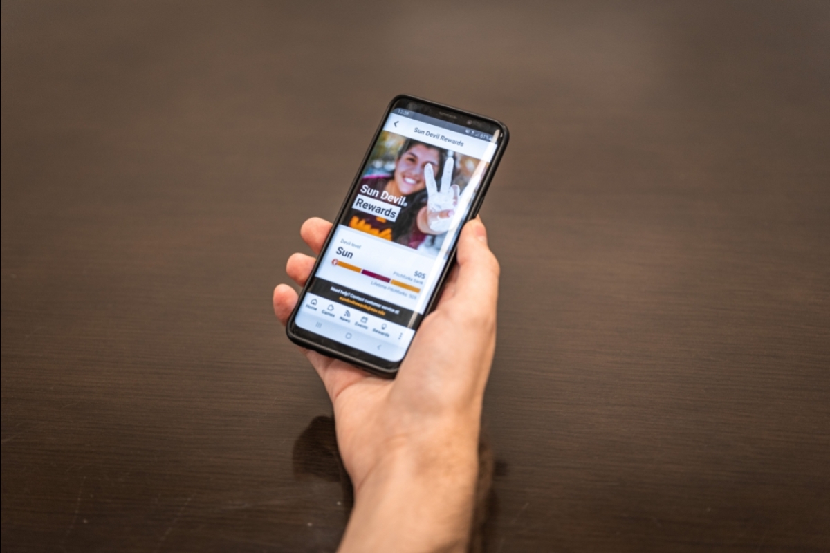 A hand holds a smart phone displaying Sun Devil Rewards in the ASU Mobile App 