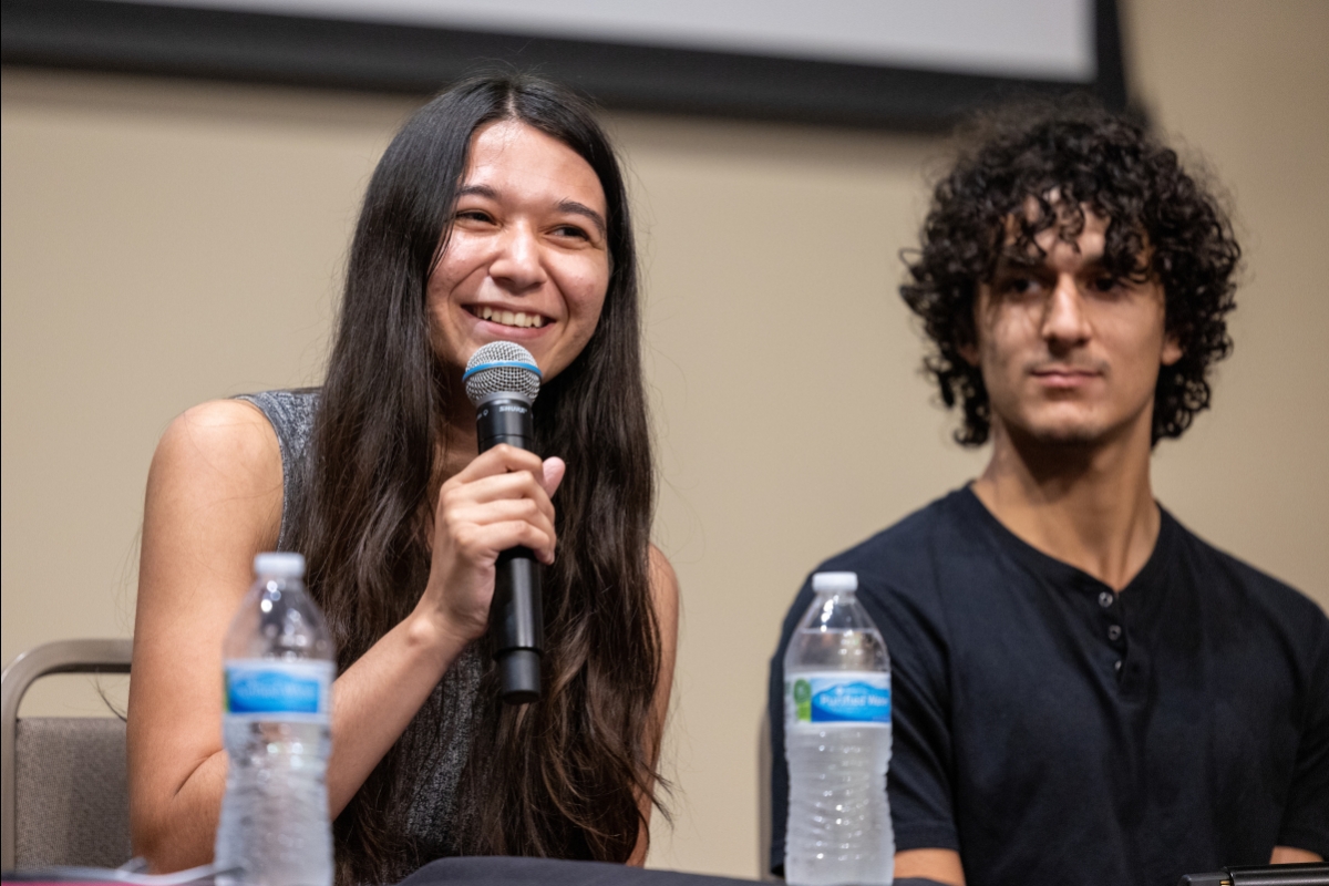 Student smiling and holding a microphone while another looks on.