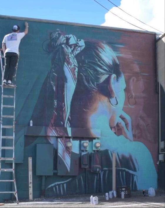 ASU alum and muralist Clyde Thompson paints a mural from a ladder