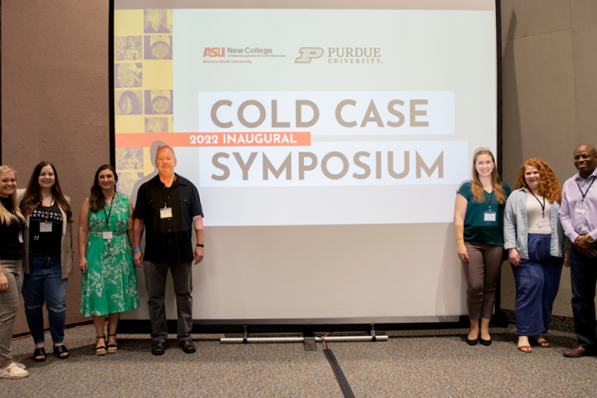 People standing on a stage on either side of a screen that reads "Cold Case Symposium."