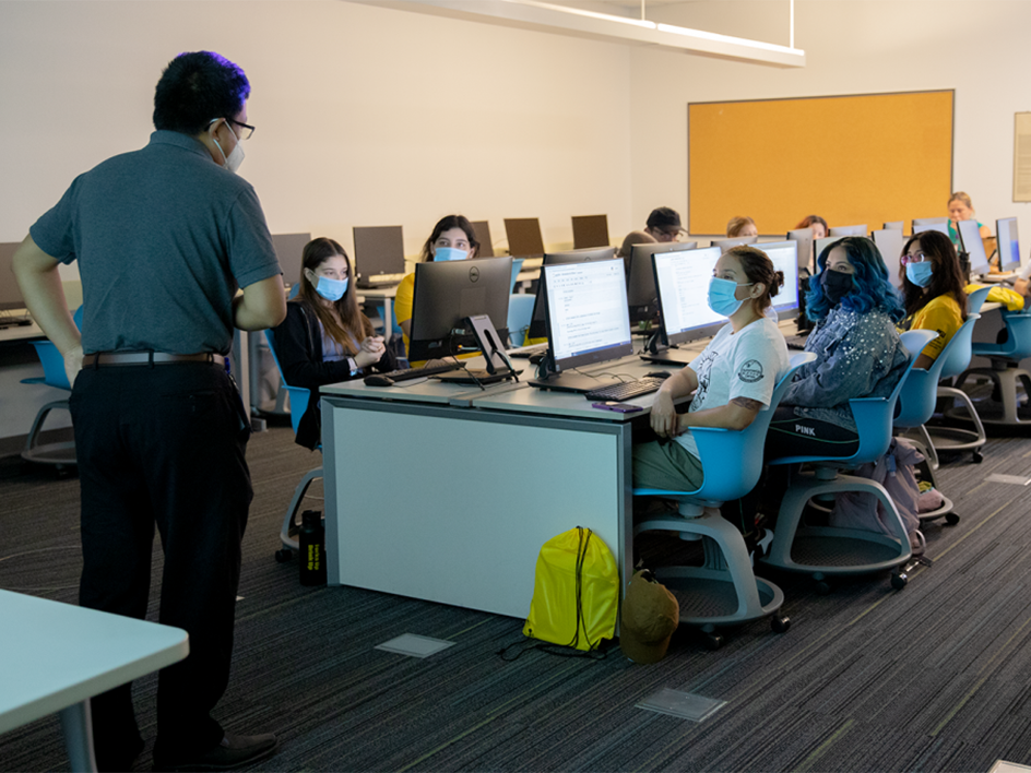 two rows of students at computers in classroom with instructor in front