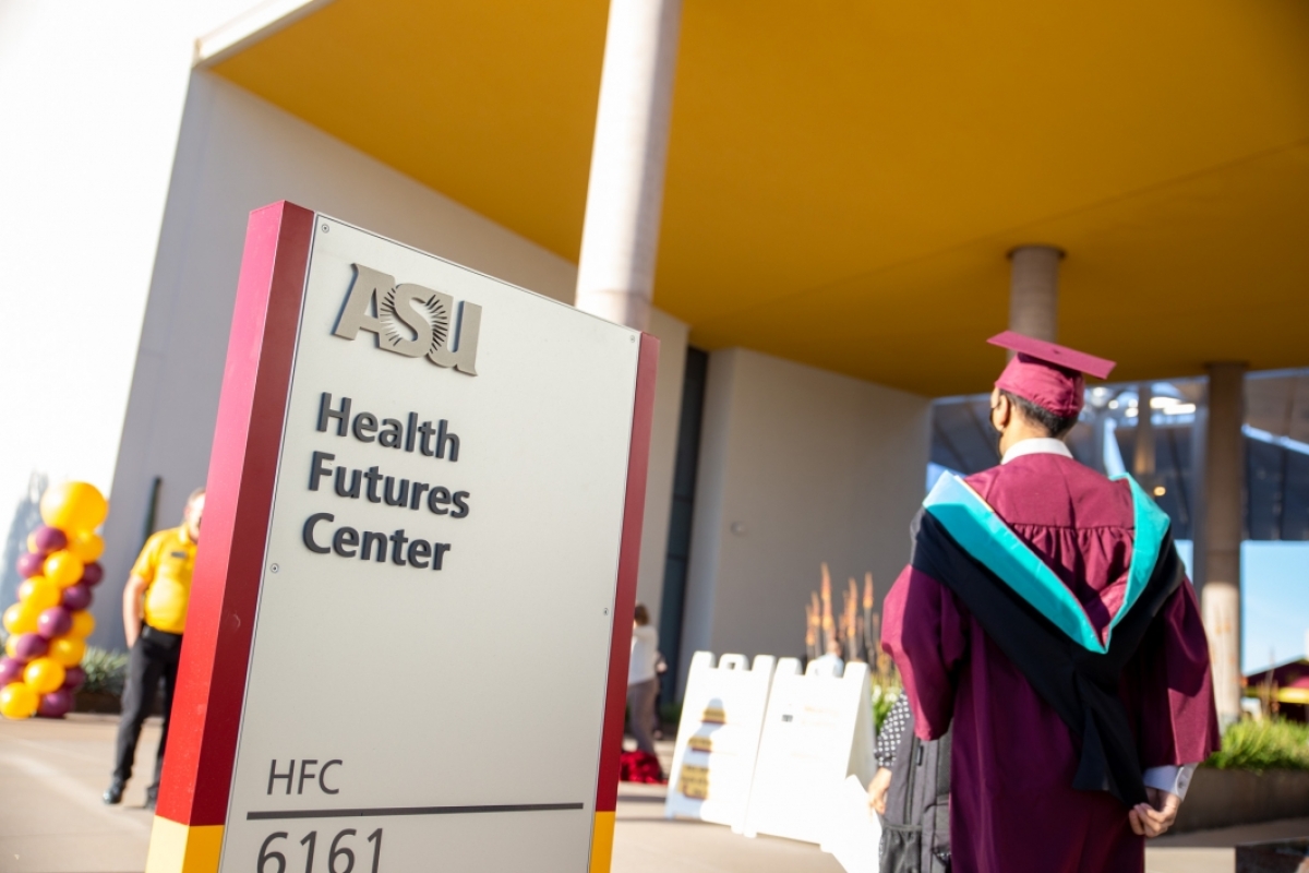 A sign reads "Health Futures Center" as a graduate walks by in their regalia.