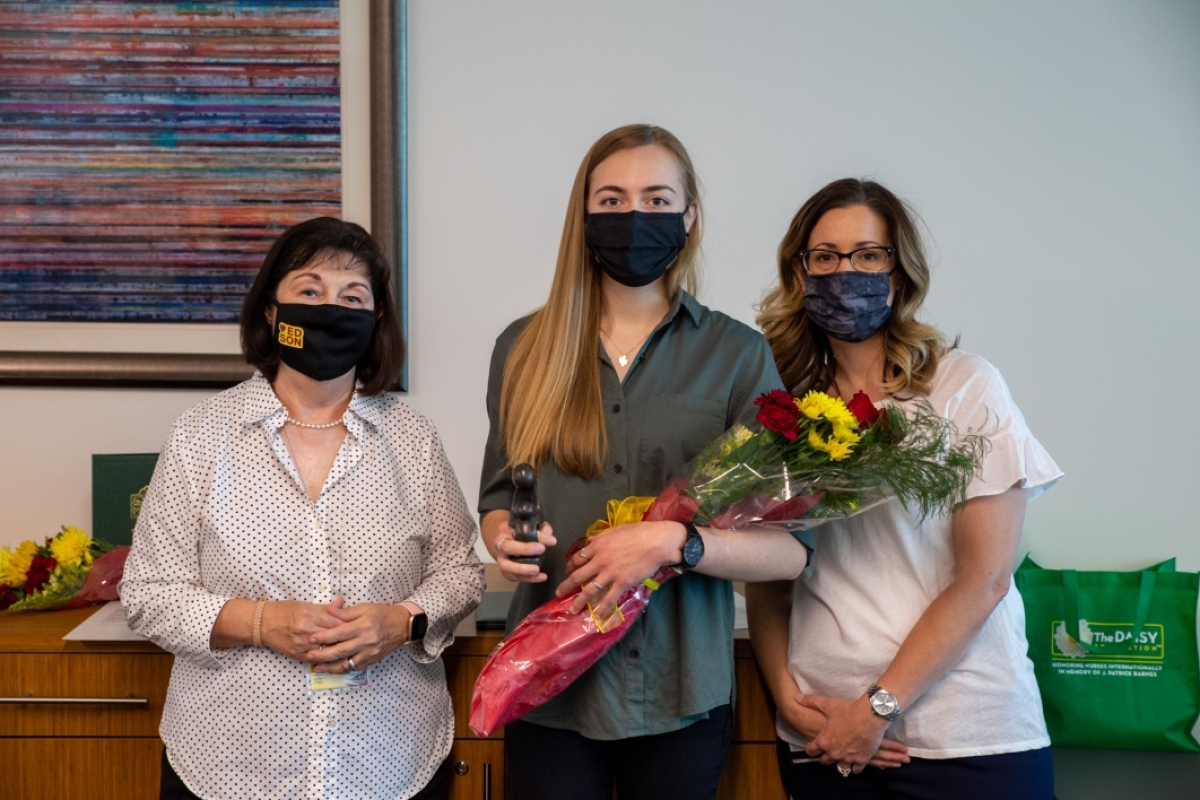 Three masked women pose for a photo, the middle one holding flowers