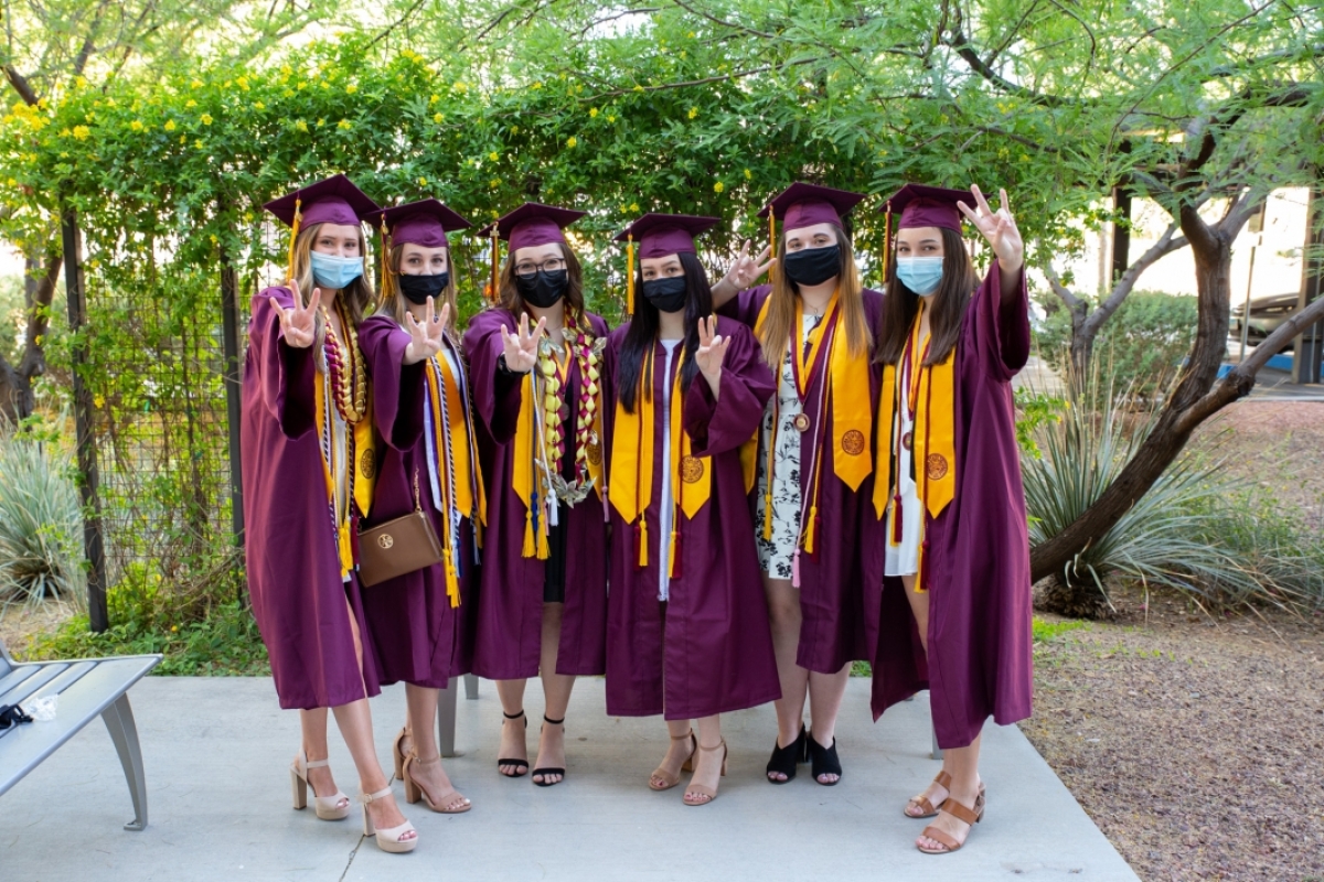 A group of women in graduation gowns pose with the pitchfork gesture