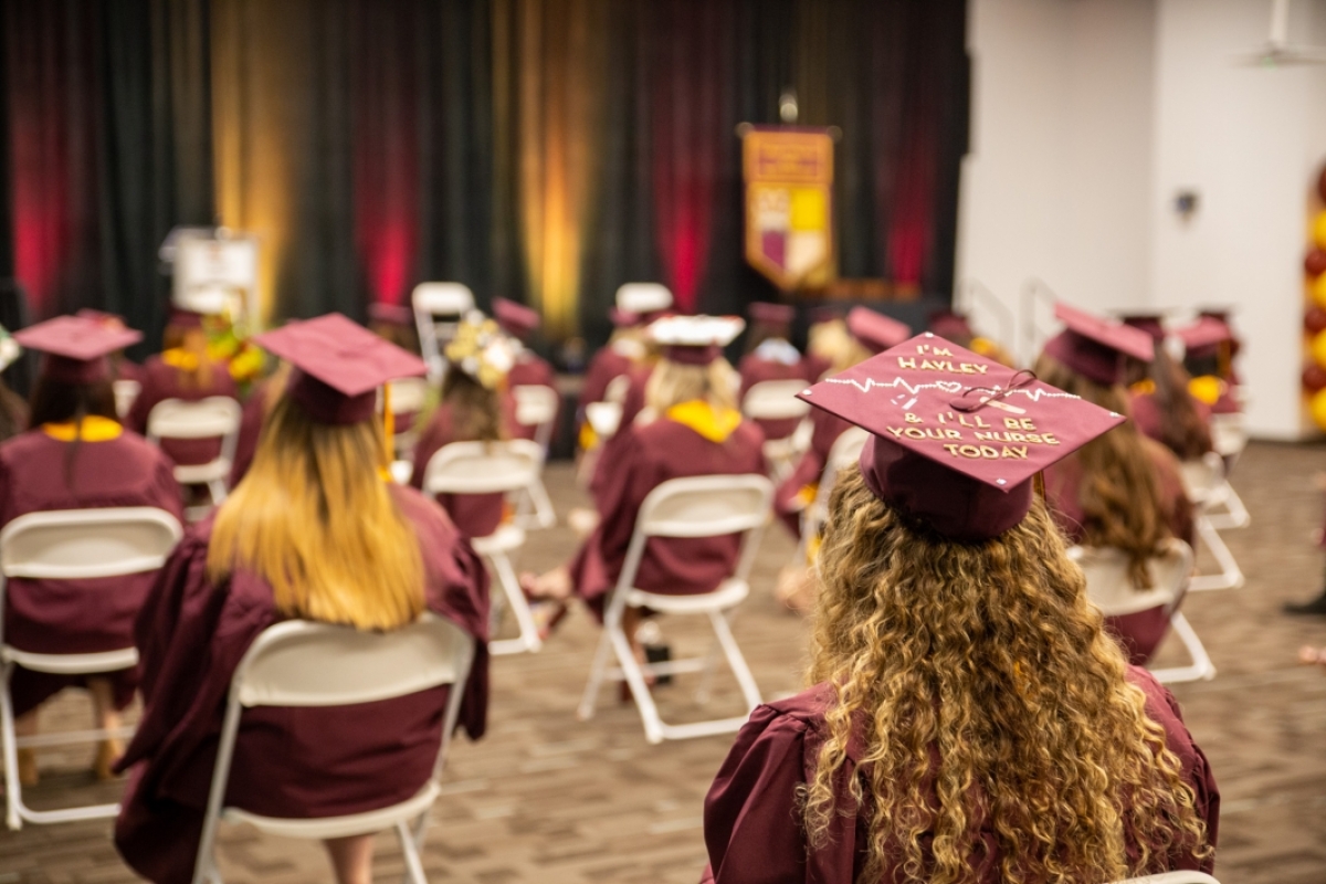 Nursing students in graduation regalia sit socially distanced in a ballroom