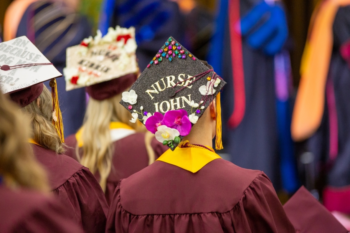 Image shows grad caps that have been decorated. The one visible says, "Nurse John"