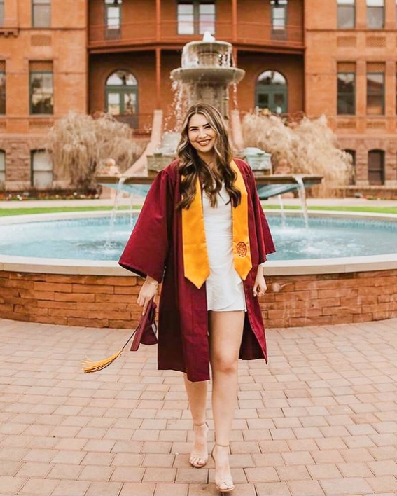 ASU College of Health Solutions graduate Maci Crookes smiling and wearing her commencement gown in front of the water fountain at Old Main on ASU's Tempe campus
