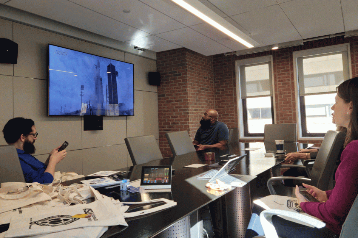 People sit around a table and watch a livestream of a NASA launch