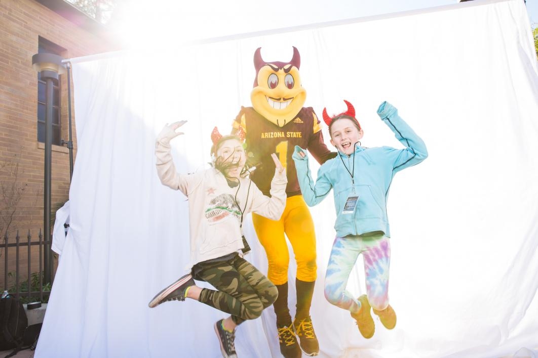 Two girls jump with Sparky in a photo-booth photo.