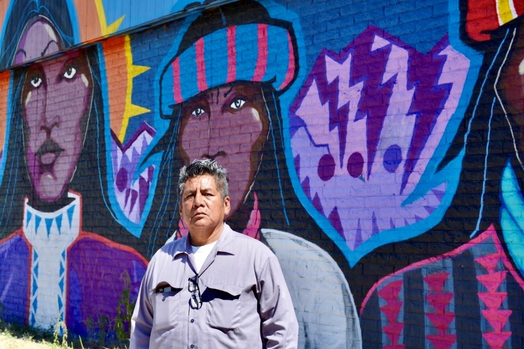 Douglas Miles standing in front of one of his murals that features three Apache figures