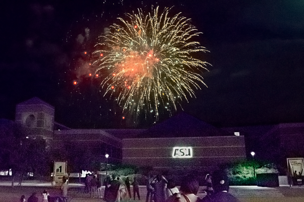 A large yellow firework explodes above a building with a sign that reads "ASU."