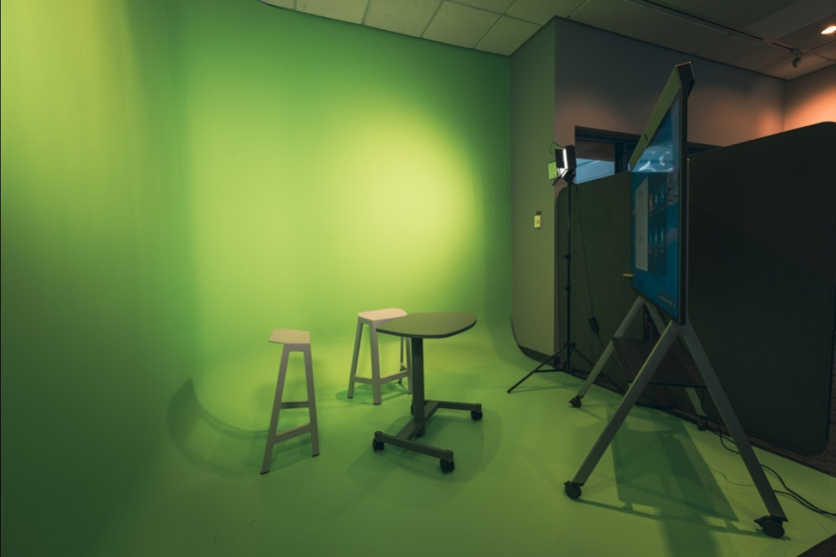 Green screen room with stools and a large video screen.