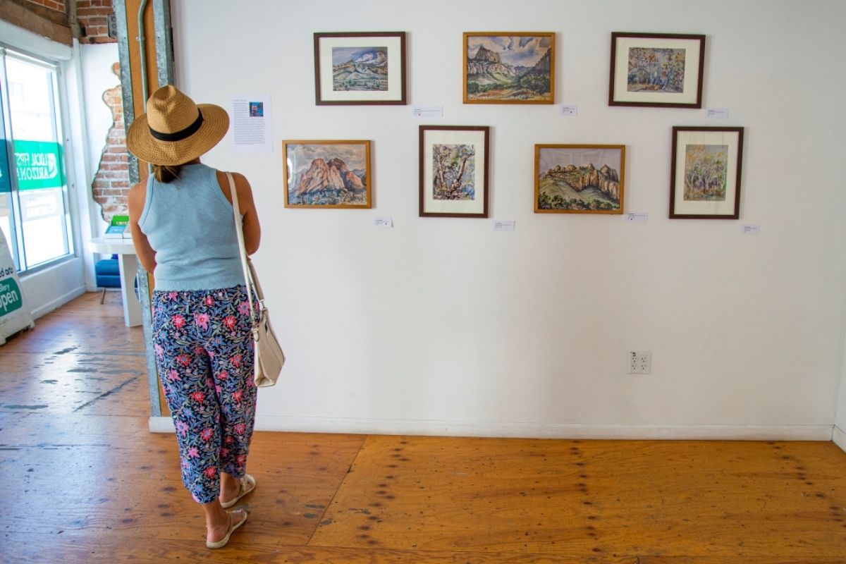 Woman in hat views display of watercolor landscape portraits at downtown gallery