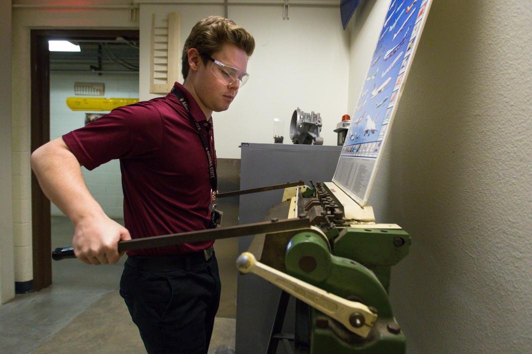 Aviation student Eamonn McIntyre bends a piece of metal in a machine.