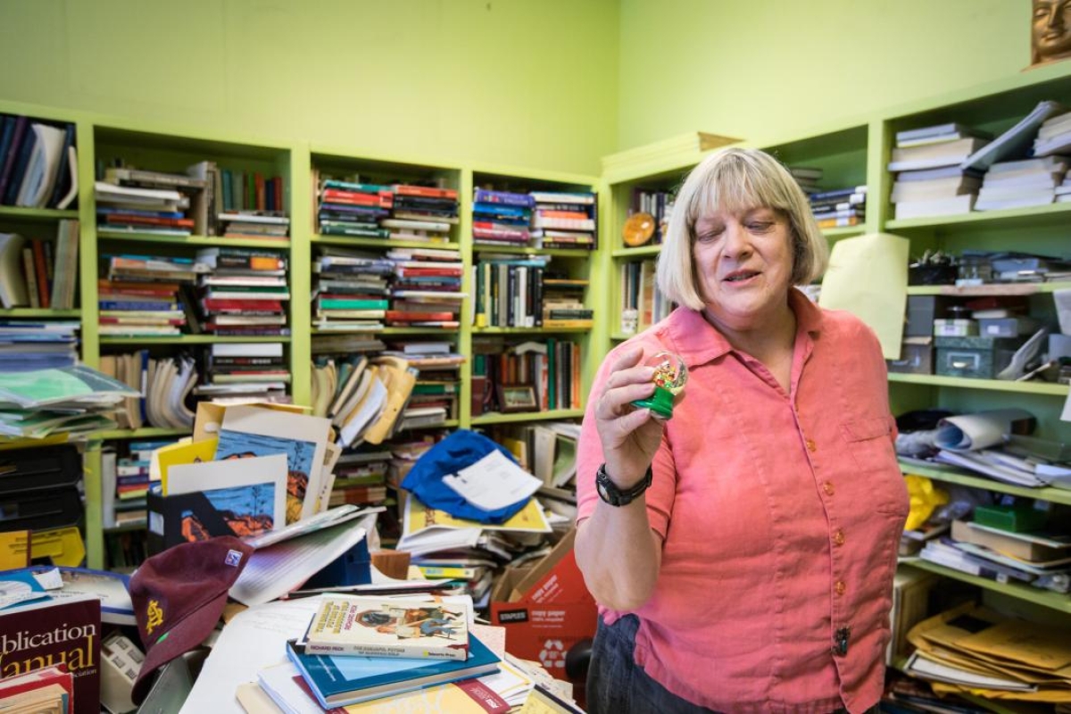 Professor Karen Adams looks at a snowglobe in her book-filled office