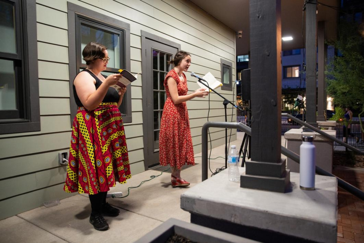 two women reading poetry into microphones on a porch