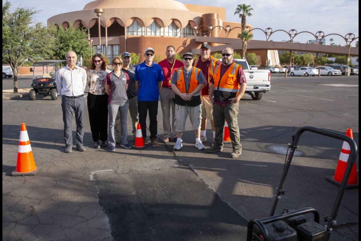 People posing for a group photo in an asphalt parking lot in front of ASU Gammage auditorium.