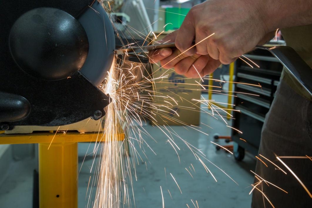 A student grinds down car parts amid a spray of sparks in the Formula SAE club's shop.
